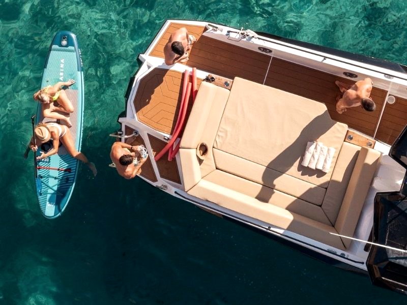 Yacht tender at anchor in clear turquoise water, guests swimming and paddleboarding