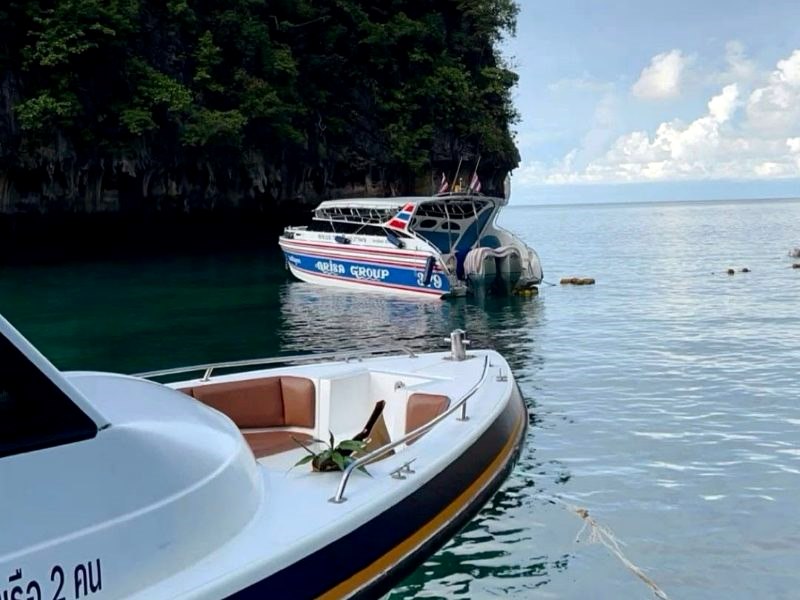 Speedboats moored in a calm bay below a jungle-covered cliff