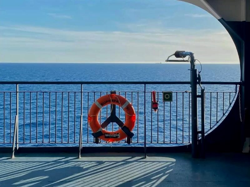 Open deck of a passenger boat with a life ring, looking out to open sea