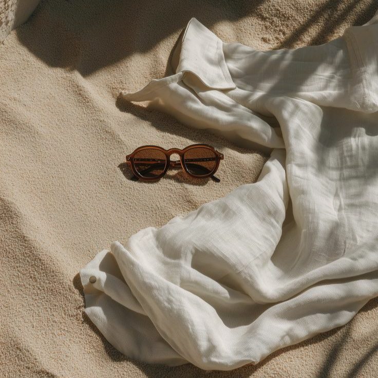 Sunglasses and a linen shirt on warm sand in palm shade