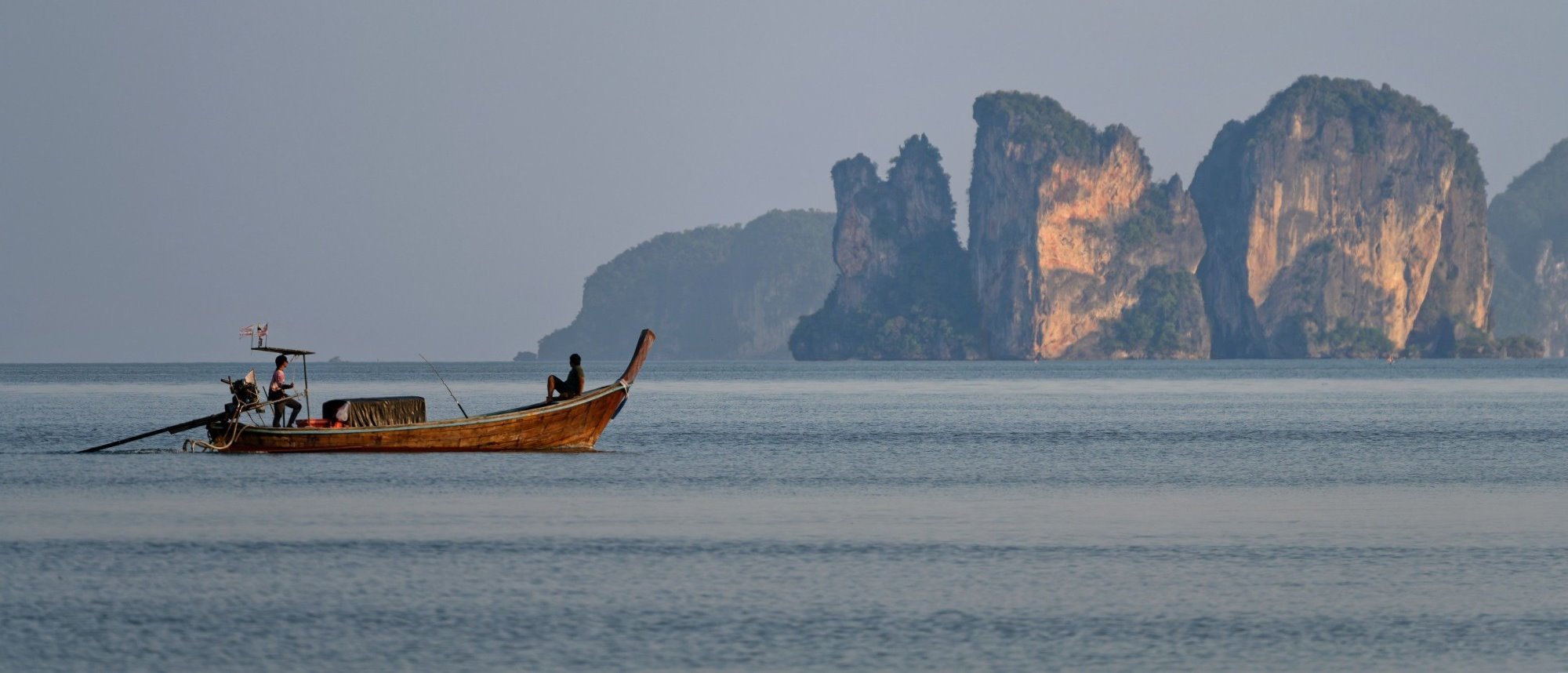 A longtail boat off Phuket at first light, limestone cliffs behind