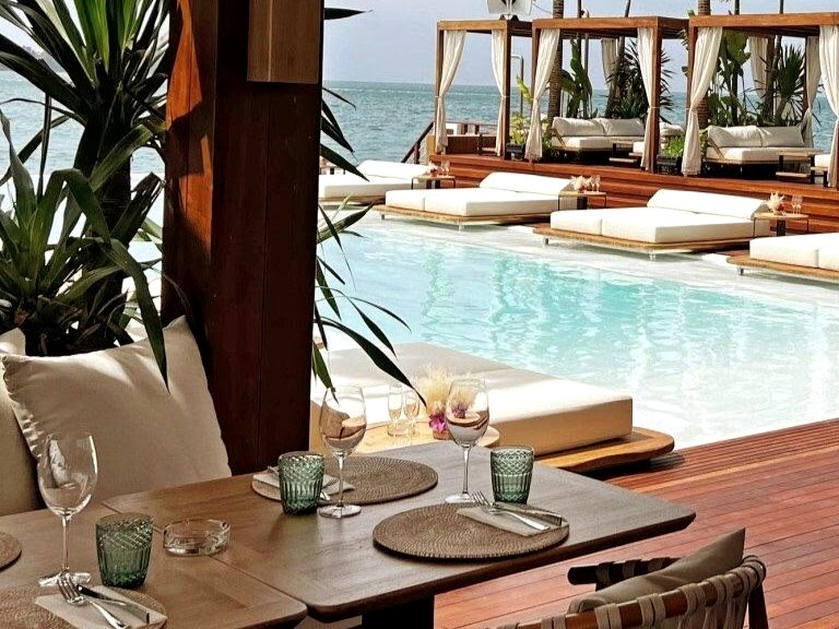Table set by a beach-club pool with cabanas and palms