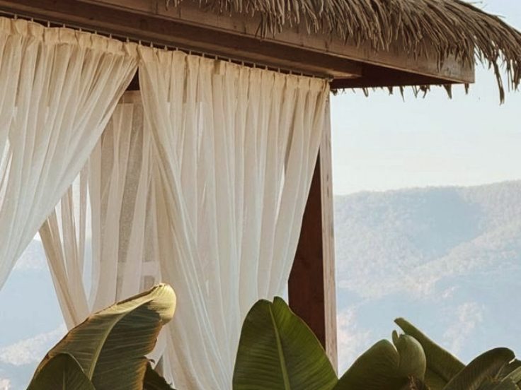 Thatched sala with white curtains among banana leaves
